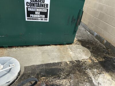 Pressure-washed concrete next to stained concrete at a shopping center dumpster area