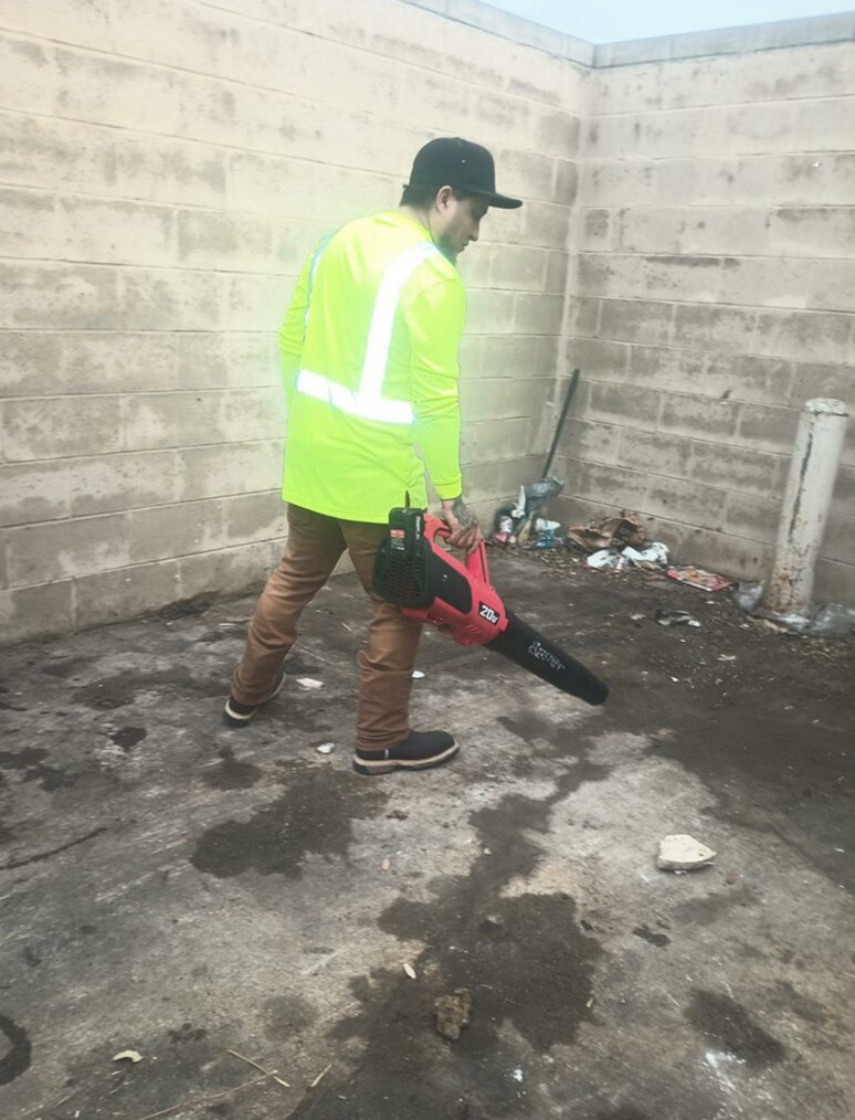 Porter blowing debris out of a retail center dumpster enclosure