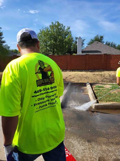 Property Zeus crew in branded safety shirts power washing a concrete curb and driveway