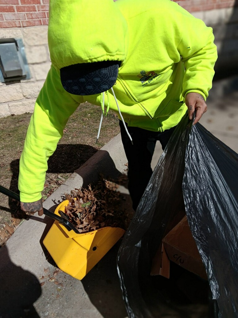 Porter bagging trash and leaves detailed out of a shopping center landscape bed