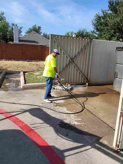 Property Zeus technician pressure washing a dumpster pad and enclosure at a DFW property